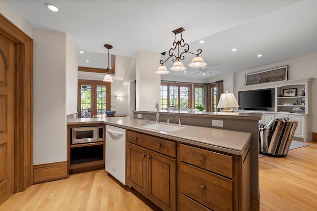 kitchen with a sink, stainless steel microwave, dishwasher, light wood-style flooring, and plenty of natural light