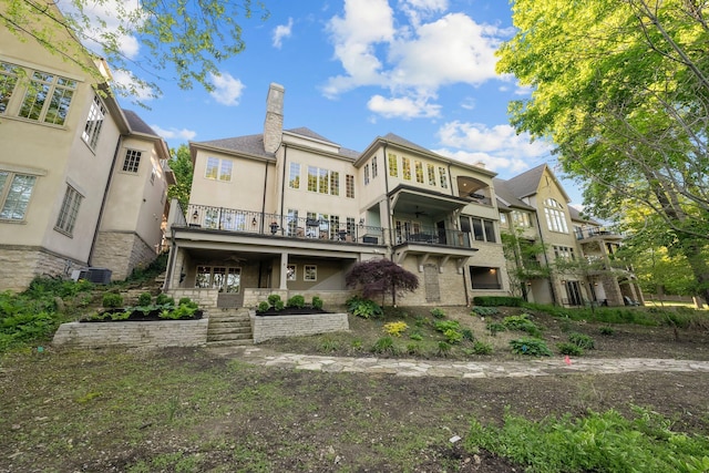 rear view of property with stucco siding, a chimney, a balcony, stone siding, and stairs