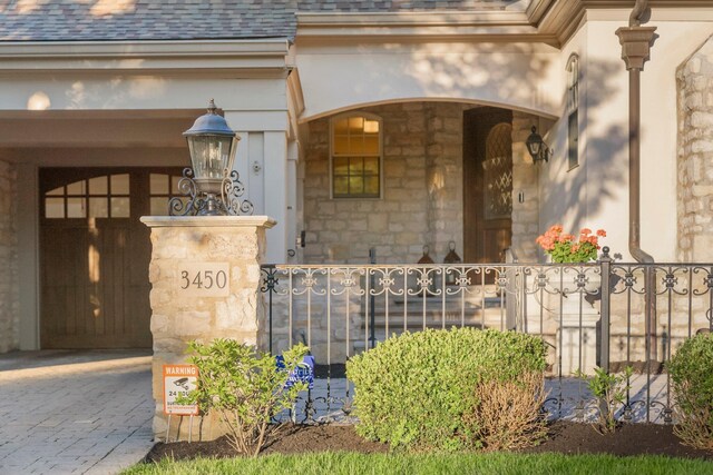 view of exterior entry featuring stone siding, fence, and roof with shingles