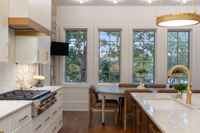 kitchen with a sink, premium range hood, stainless steel gas stovetop, white cabinetry, and light stone counters