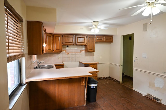 kitchen with ceiling fan, a peninsula, a sink, brown cabinets, and tasteful backsplash