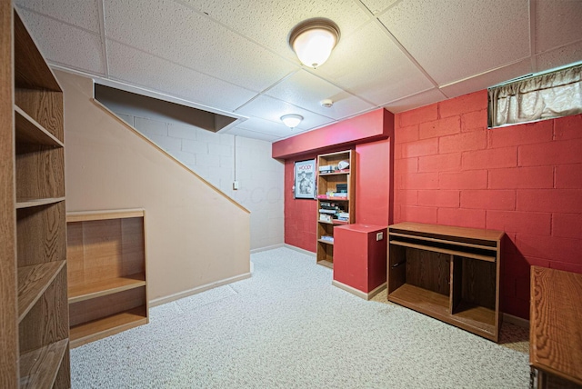 finished below grade area featuring a paneled ceiling, carpet flooring, concrete block wall, stairway, and baseboards