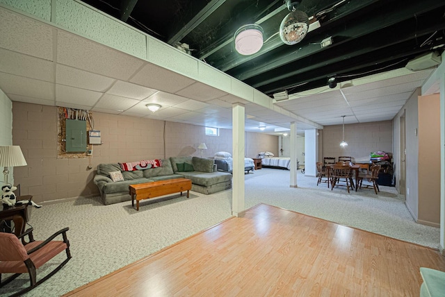 living area with electric panel, wood finished floors, concrete block wall, and a drop ceiling