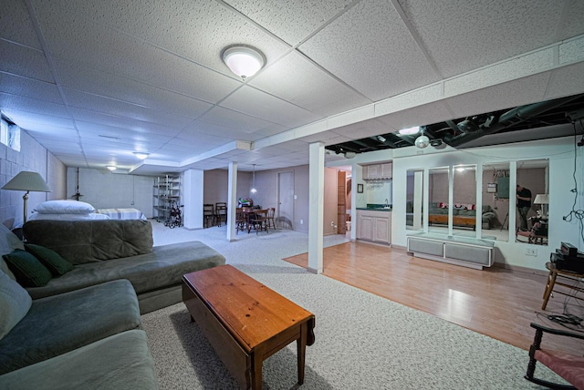 carpeted living room with a paneled ceiling, wood finished floors, and baseboards