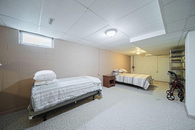 bedroom with a paneled ceiling, carpet floors, and concrete block wall