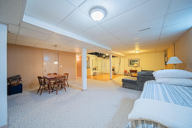 carpeted bedroom with concrete block wall and a drop ceiling