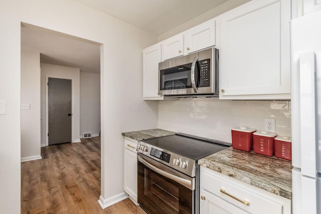 kitchen with stainless steel appliances, decorative backsplash, white cabinets, light wood-style floors, and baseboards