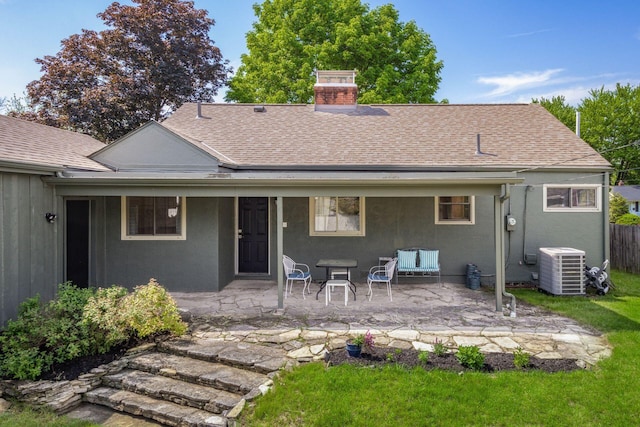 rear view of property featuring a shingled roof, a chimney, stucco siding, central air condition unit, and a patio area