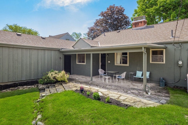 back of house featuring a patio area, a chimney, a yard, roof with shingles, and stucco siding