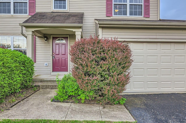 entrance to property featuring an attached garage and roof with shingles