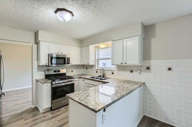 kitchen featuring stainless steel appliances, a sink, light wood finished floors, light stone countertops, and a peninsula