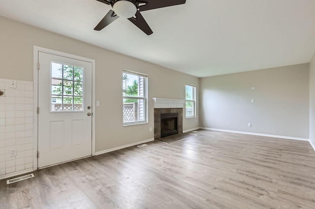unfurnished living room featuring plenty of natural light, wood finished floors, ceiling fan, and a tiled fireplace