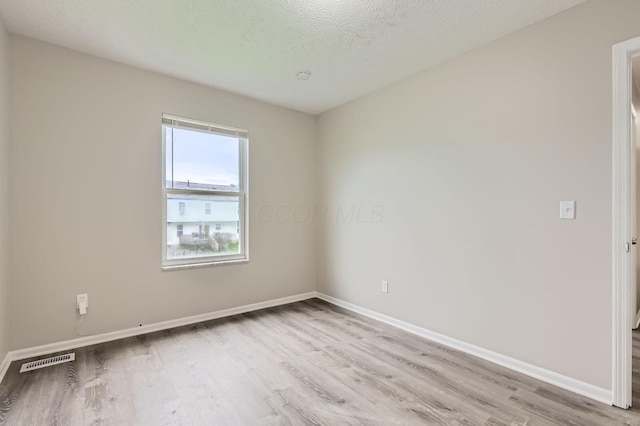 unfurnished room with light wood finished floors, baseboards, and a textured ceiling