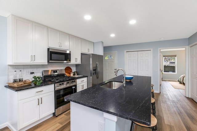 225 Reeb Ave, Columbus, OH 43207 - kitchen featuring appliances with stainless steel finishes, light wood-style flooring, tasteful backsplash, a center island with sink, and a breakfast bar