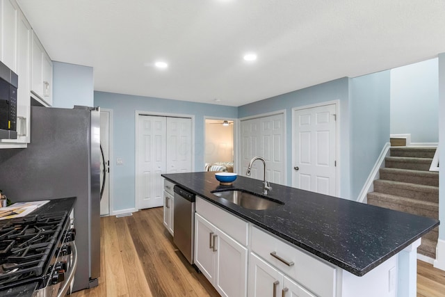 225 Reeb Ave, Columbus, OH 43207 - kitchen featuring appliances with stainless steel finishes, light wood-style floors, white cabinets, dark stone counters, and a center island with sink