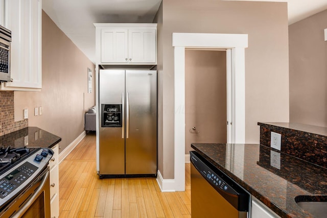 kitchen featuring stainless steel appliances, light wood-type flooring, white cabinets, backsplash, and dark stone counters