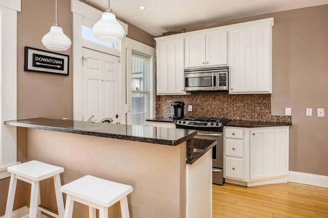 204-206 E Blenkner St, Columbus, OH 43206 - kitchen with stainless steel appliances, backsplash, light wood-style flooring, white cabinetry, and a kitchen bar