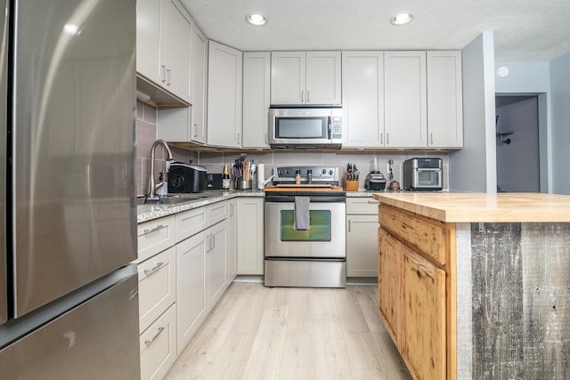 2806 Claude Dr, Columbus, OH 43207 - kitchen featuring appliances with stainless steel finishes, a sink, butcher block countertops, light wood-style flooring, and tasteful backsplash