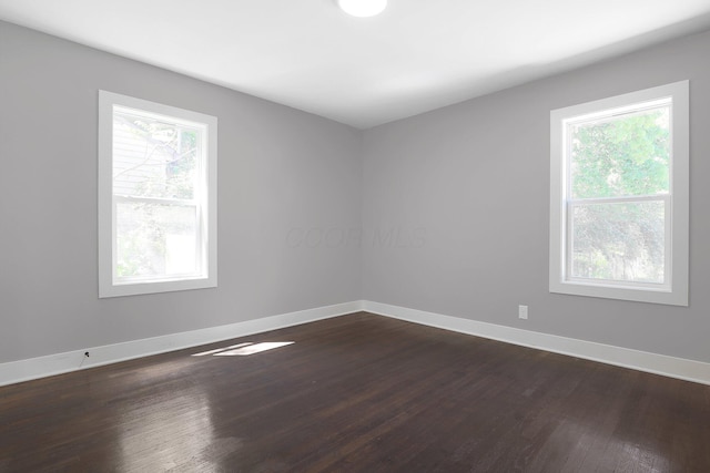 unfurnished room featuring plenty of natural light, dark wood-type flooring, and baseboards