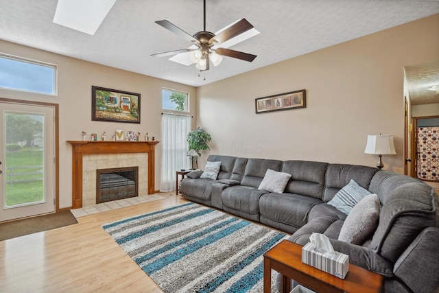 890 Brockwell Dr, Westerville, OH 43081 - living room featuring light wood-type flooring, a ceiling fan, a textured ceiling, a tiled fireplace, and a skylight