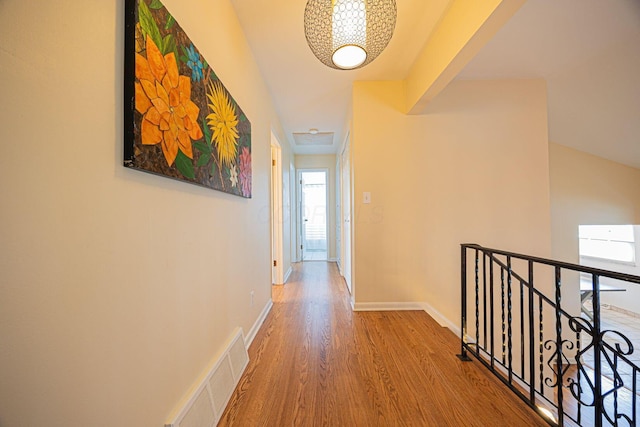 hall with an upstairs landing, healthy amount of natural light, wood finished floors, and baseboards
