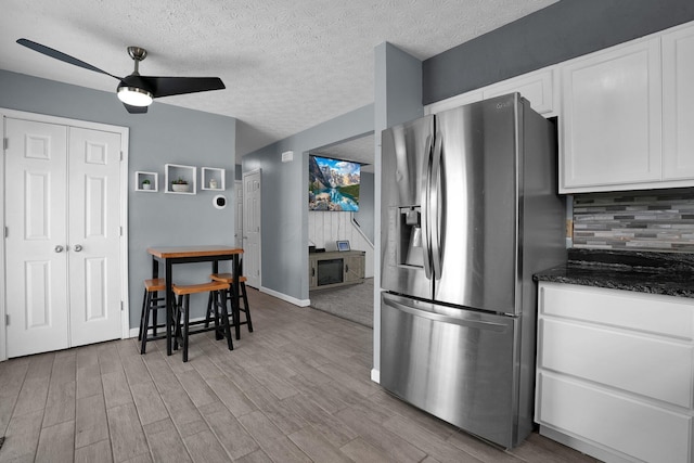 kitchen with stainless steel refrigerator with ice dispenser, a ceiling fan, white cabinetry, tasteful backsplash, and wood finished floors