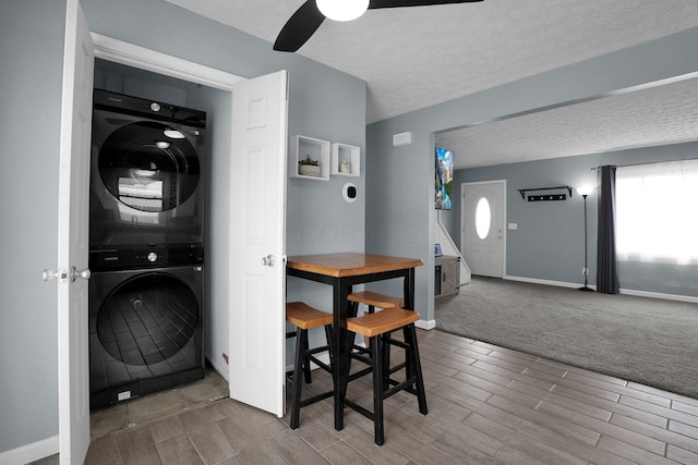 clothes washing area featuring stacked washing machine and dryer, wood finish floors, a ceiling fan, a textured ceiling, and baseboards