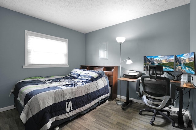 bedroom featuring wood finished floors, baseboards, a textured ceiling, an office area, and electric panel