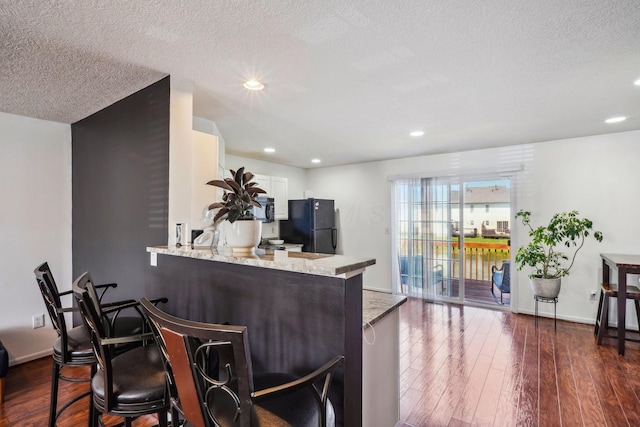 kitchen with black appliances, a peninsula, dark wood finished floors, light stone counters, and recessed lighting