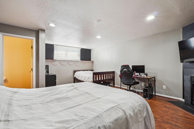 bedroom featuring wood finished floors, recessed lighting, baseboards, a fireplace with flush hearth, and a textured ceiling