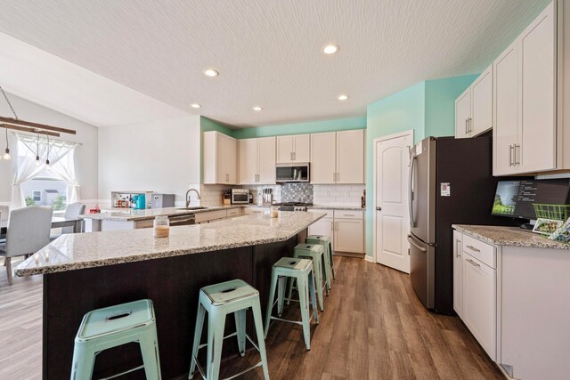 331 Hardwood Ave, Circleville, OH 43113 - kitchen featuring appliances with stainless steel finishes, a breakfast bar, backsplash, wood finished floors, and light stone countertops