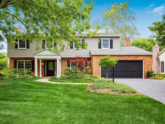 colonial inspired home featuring asphalt driveway, a chimney, brick siding, a garage, and a front yard