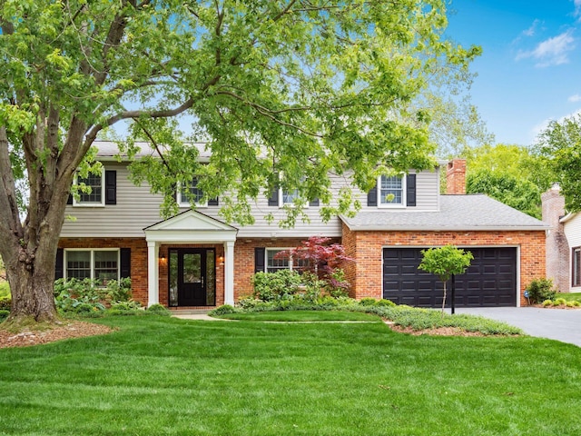 view of front facade featuring a front lawn, driveway, brick siding, a chimney, and a shingled roof