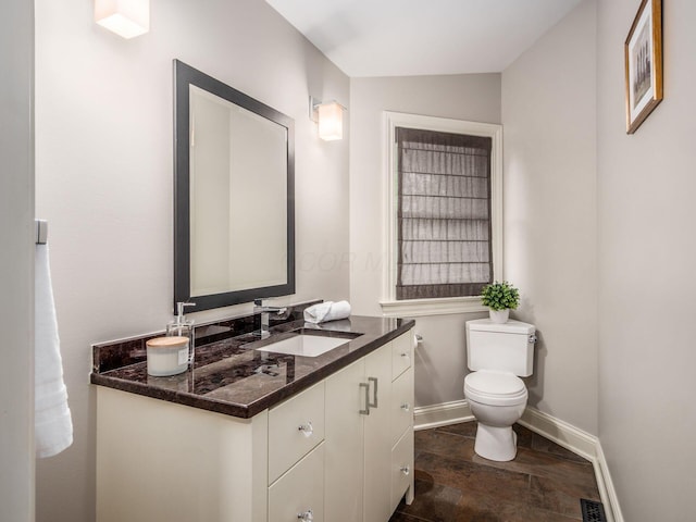 half bathroom with baseboards, toilet, vanity, and stone finish flooring