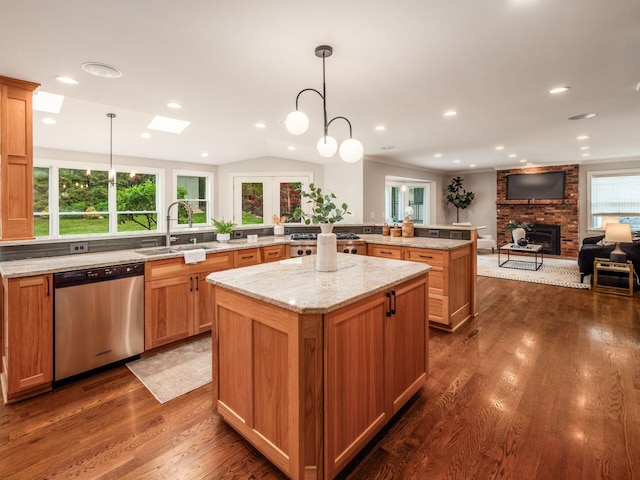 kitchen with stainless steel dishwasher, a sink, a brick fireplace, a kitchen island, and a skylight