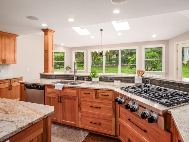 kitchen with appliances with stainless steel finishes, a sink, a skylight, light stone countertops, and wood finished floors