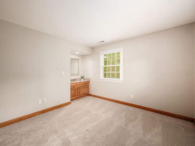 unfurnished room featuring baseboards, light carpet, and a sink