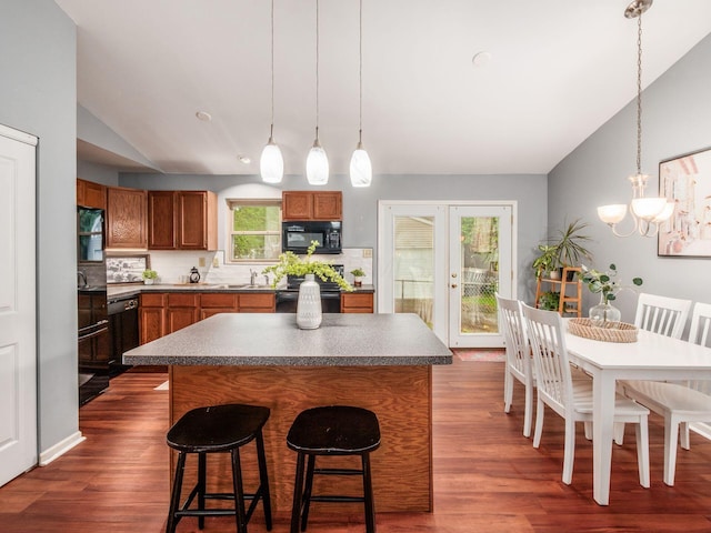 kitchen featuring black appliances, brown cabinets, vaulted ceiling, a kitchen bar, and dark wood-type flooring