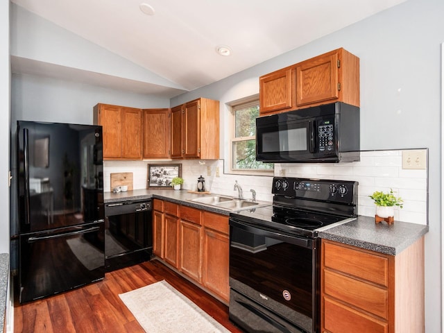 kitchen with black appliances, a sink, dark wood-style flooring, vaulted ceiling, and dark countertops