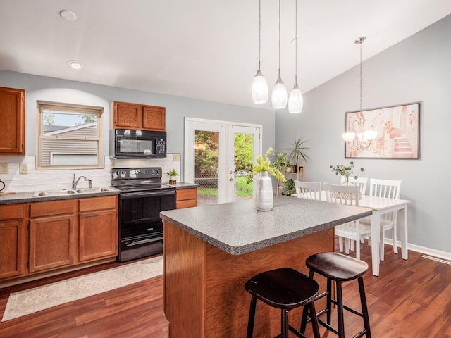 kitchen featuring black appliances, a sink, brown cabinets, a breakfast bar, and vaulted ceiling