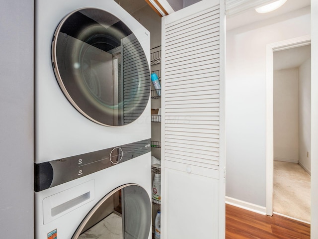 washroom featuring stacked washer and clothes dryer, baseboards, and wood finished floors