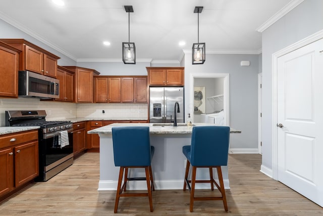 243 Parkgate Ct, Delaware, OH 43015 - kitchen with stainless steel appliances, brown cabinets, decorative backsplash, a kitchen island with sink, and crown molding