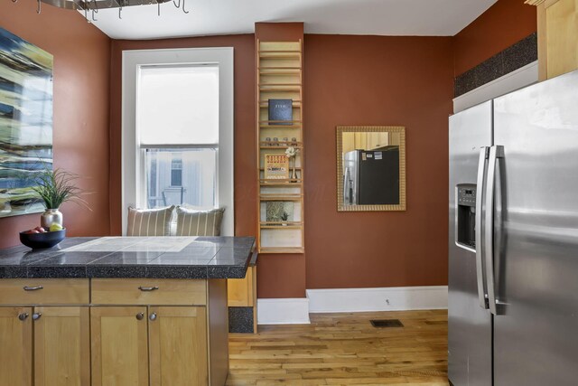 1041 Franklin Ave, Columbus, OH 43205 - kitchen featuring stainless steel refrigerator with ice dispenser, tile counters, light wood-style flooring, and baseboards