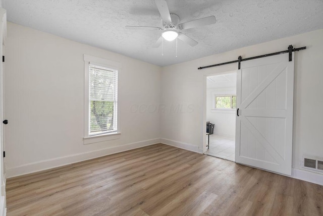 357 E Welch Ave, Columbus, OH 43207 - empty room featuring light wood-style floors, a barn door, ceiling fan, a textured ceiling, and baseboards