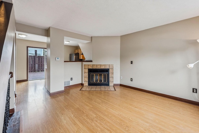 unfurnished living room featuring wood finished floors, a fireplace, baseboards, and a textured ceiling