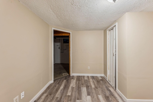 unfurnished bedroom featuring a textured ceiling, a closet, wood finished floors, and baseboards
