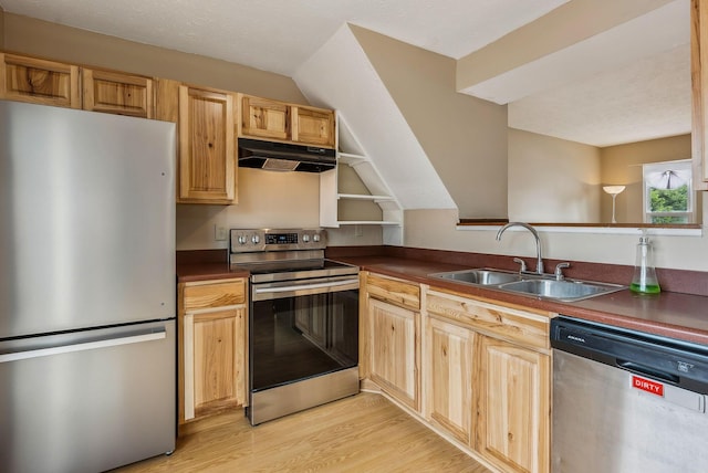 kitchen with appliances with stainless steel finishes, under cabinet range hood, a sink, dark countertops, and light wood-style floors