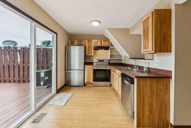 kitchen with stainless steel appliances, a sink, under cabinet range hood, dark countertops, and light wood-style flooring