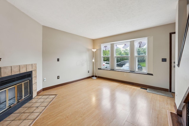 unfurnished living room with wood finished floors, a fireplace, baseboards, and a textured ceiling