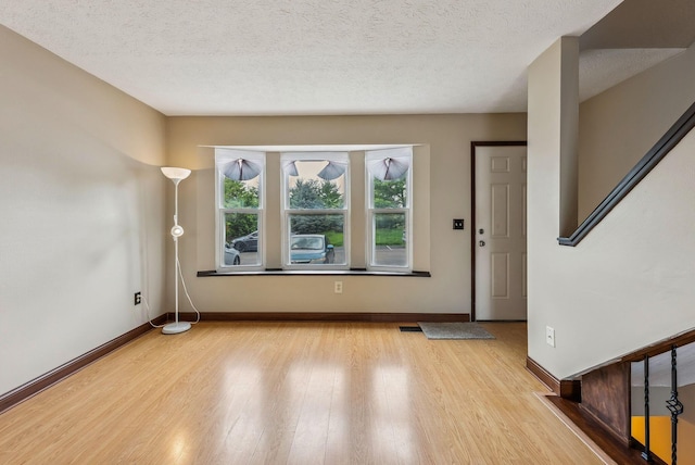 entryway featuring light wood finished floors, baseboards, stairway, and a textured ceiling